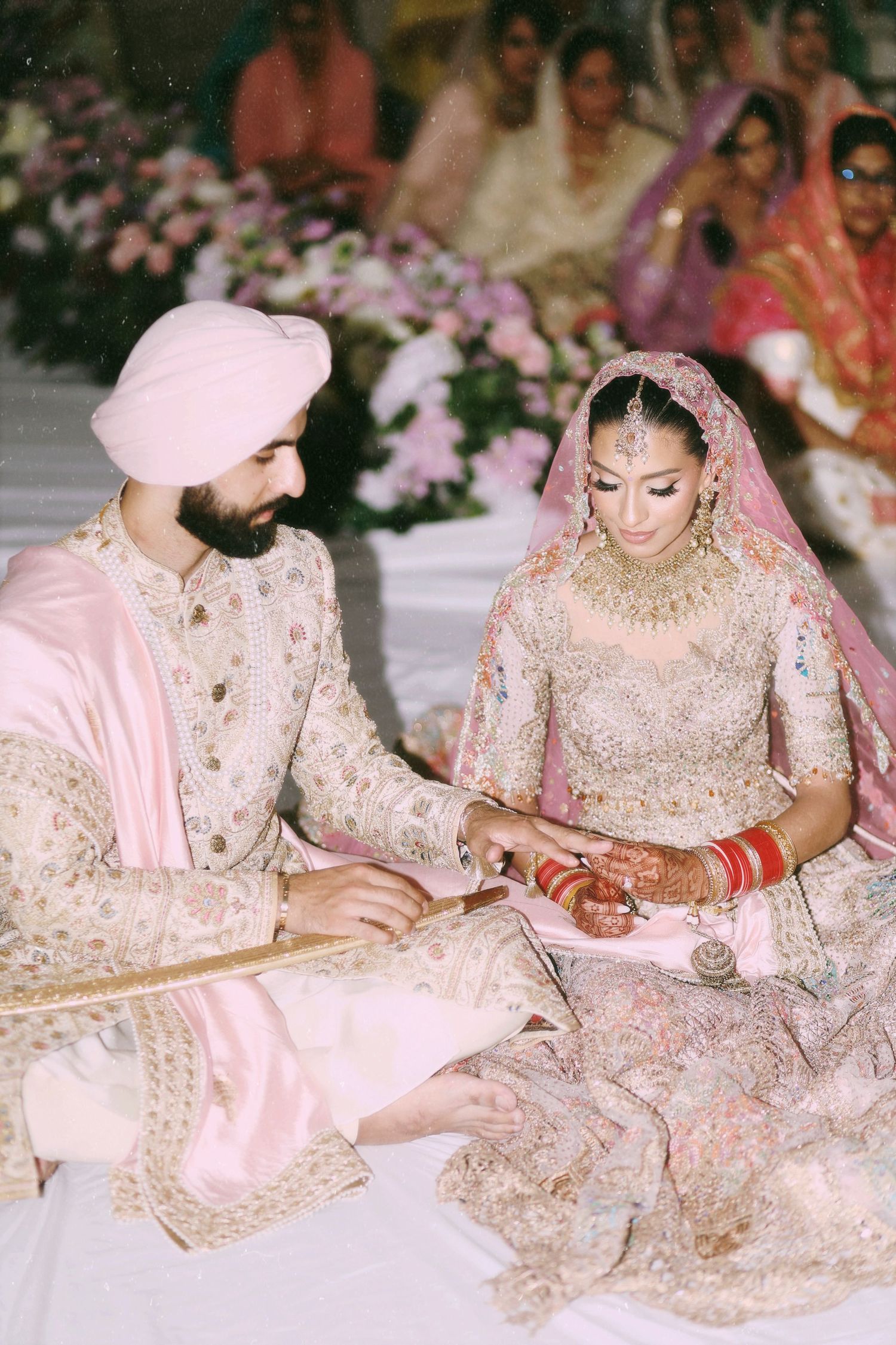 Traditional Sikh wedding ceremony with couple in elegant pink and cream outfits during ritual.