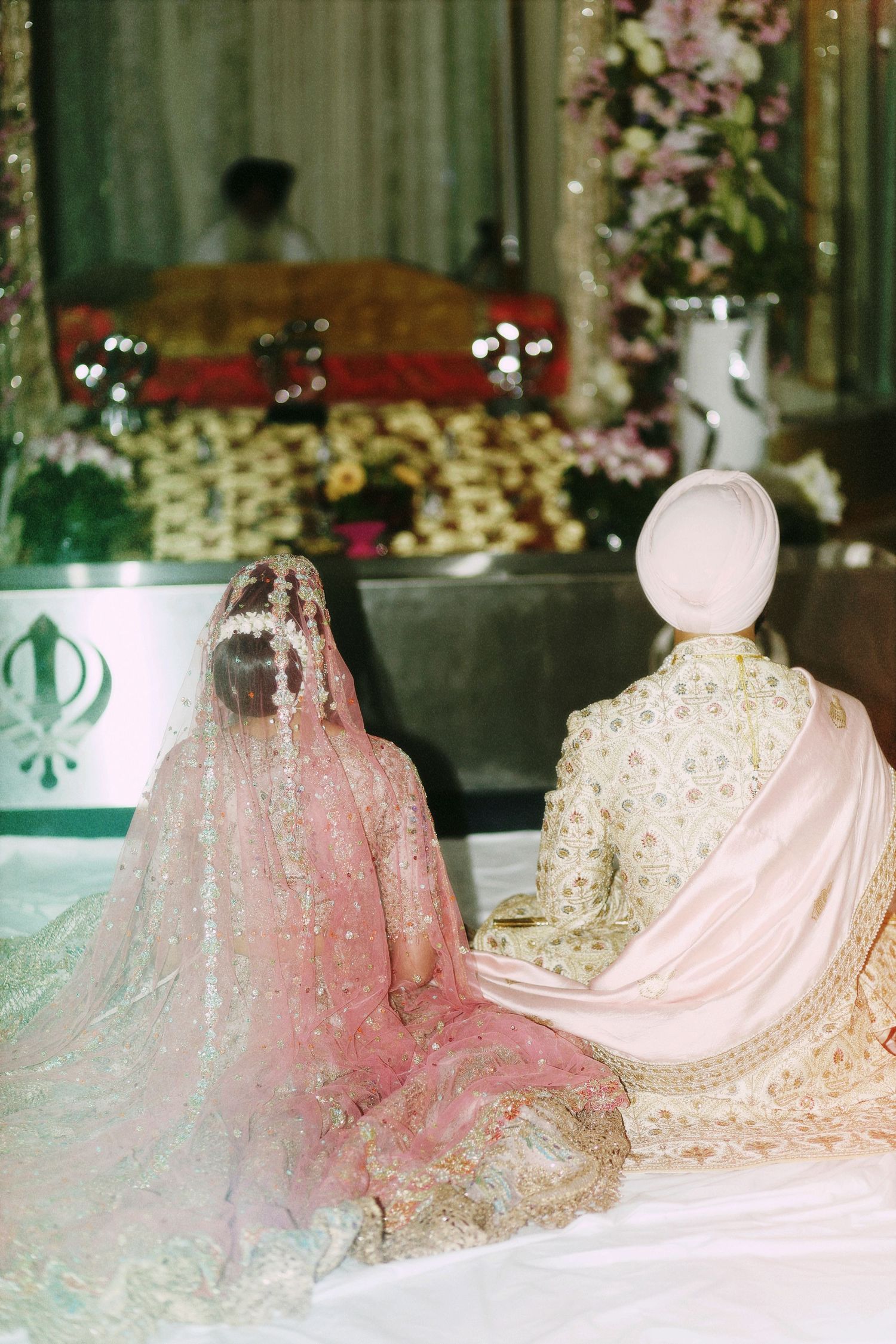 Wedding couple in traditional Sikh ceremony attire viewed from behind.