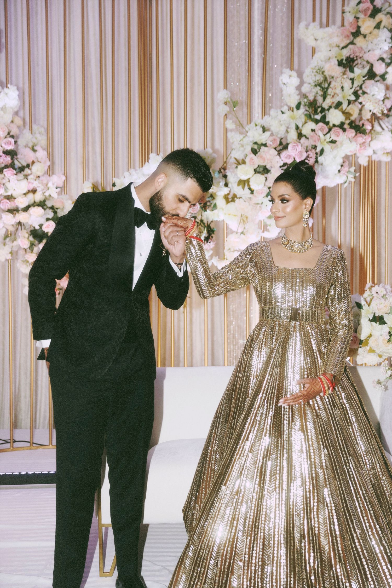 A couple in formal attire shares a romantic moment against a floral backdrop.