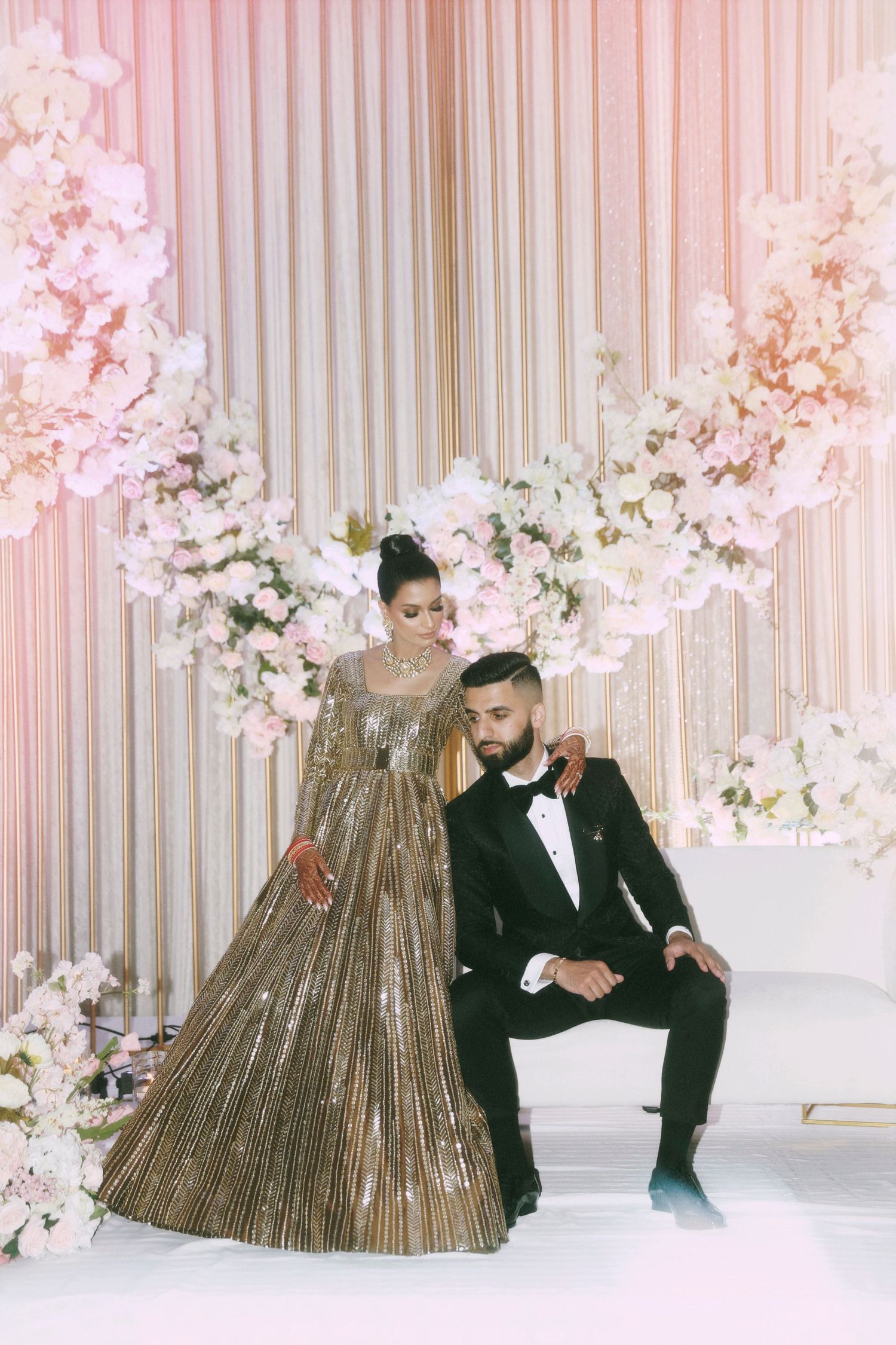 A couple poses against a floral backdrop in glamorous evening wear.