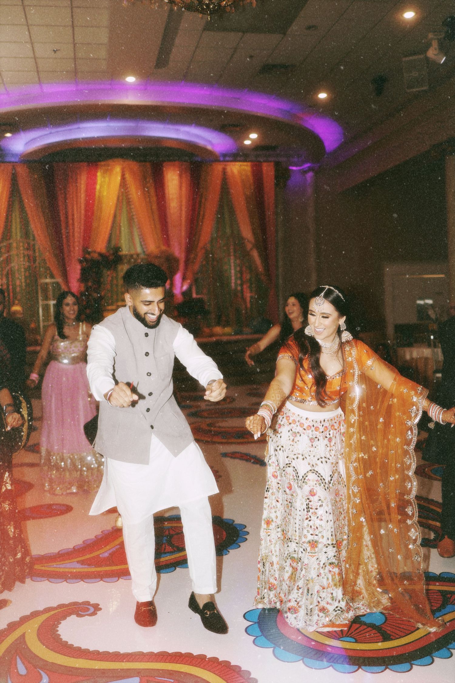 A couple dancing together at an Indian wedding reception on a decoratively patterned floor.