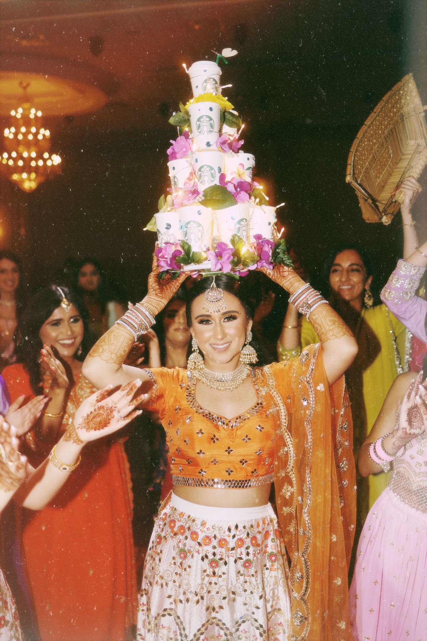 A person wearing traditional Indian attire balances a decorated cake on their head during a celebration.