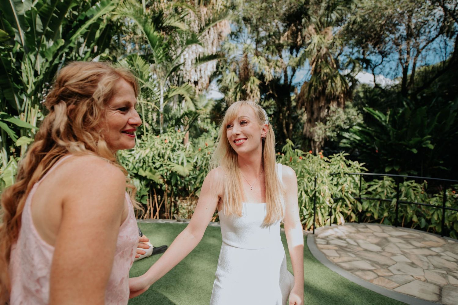 Wedding guests share joyful moments in a tropical garden setting with lush greenery.