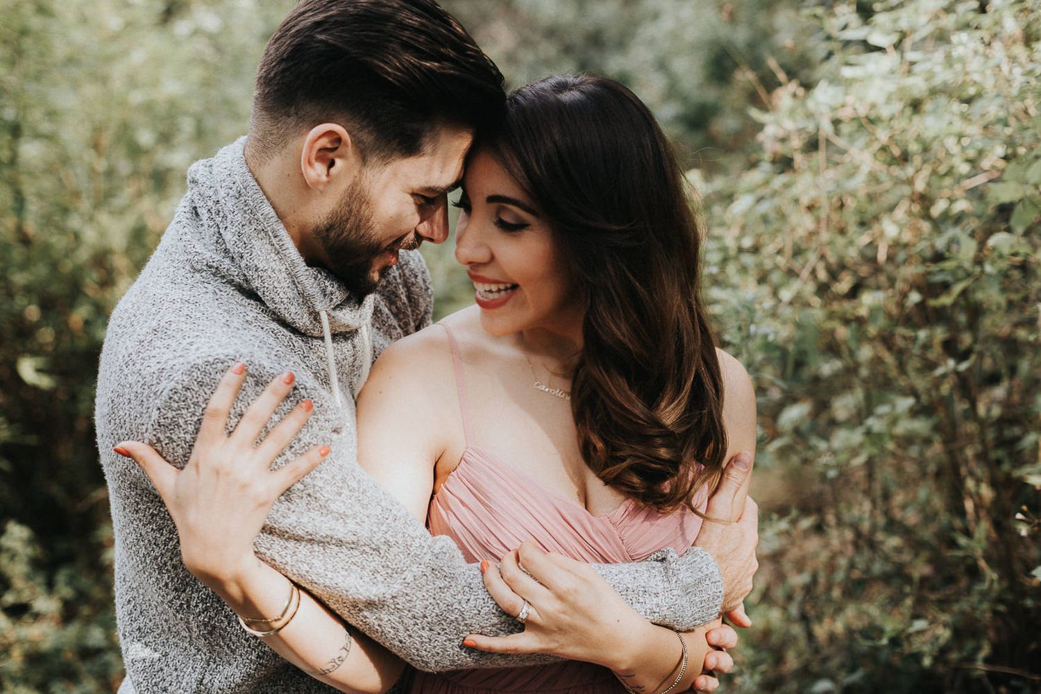 Romantic couple in casual wear embracing outdoors against a natural green background.
