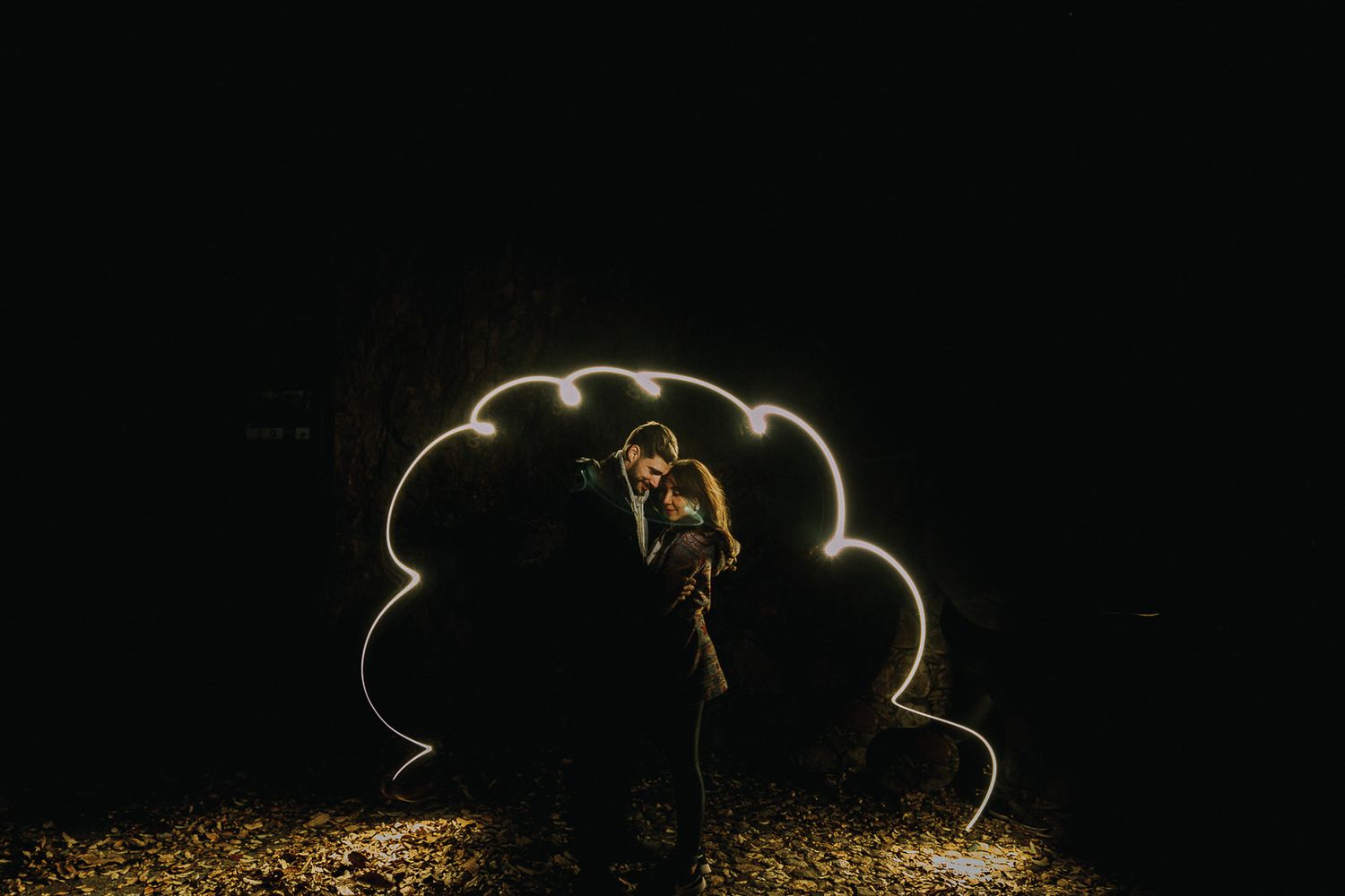 Couple silhouetted against illuminated string lights forming a cloud shape at night.
