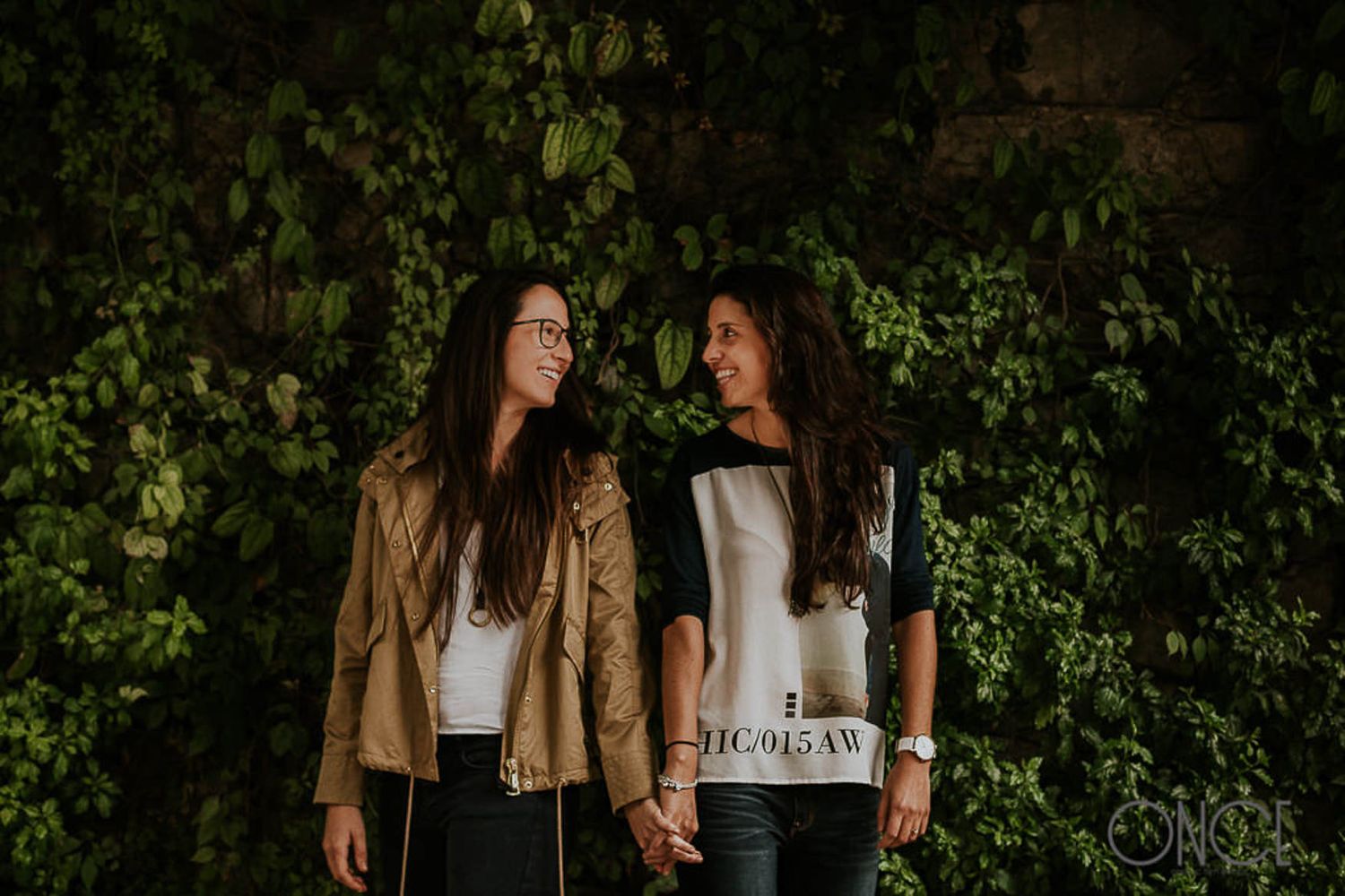 Two people in casual attire standing together against an ivy-covered wall.