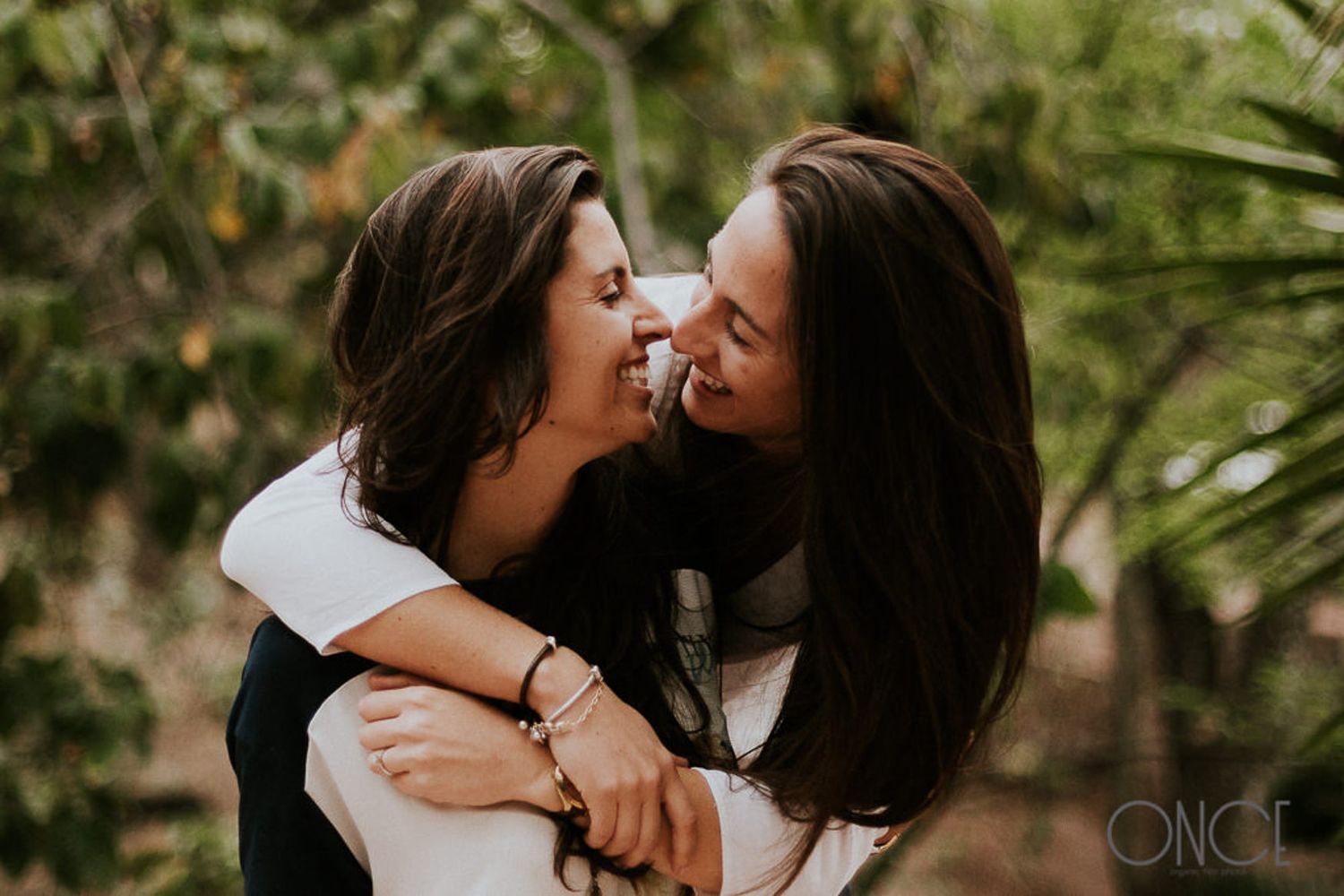 Two people sharing a joyful embrace against a tropical green background.