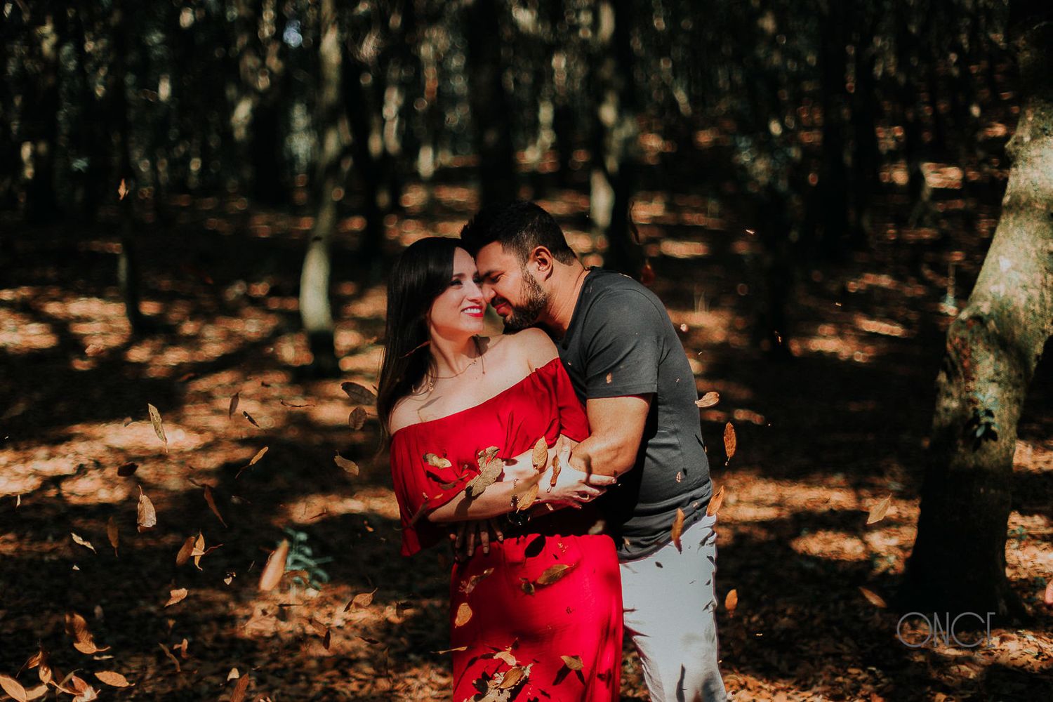 Romantic couple embracing in a sunlit forest, woman wearing vibrant red dress.