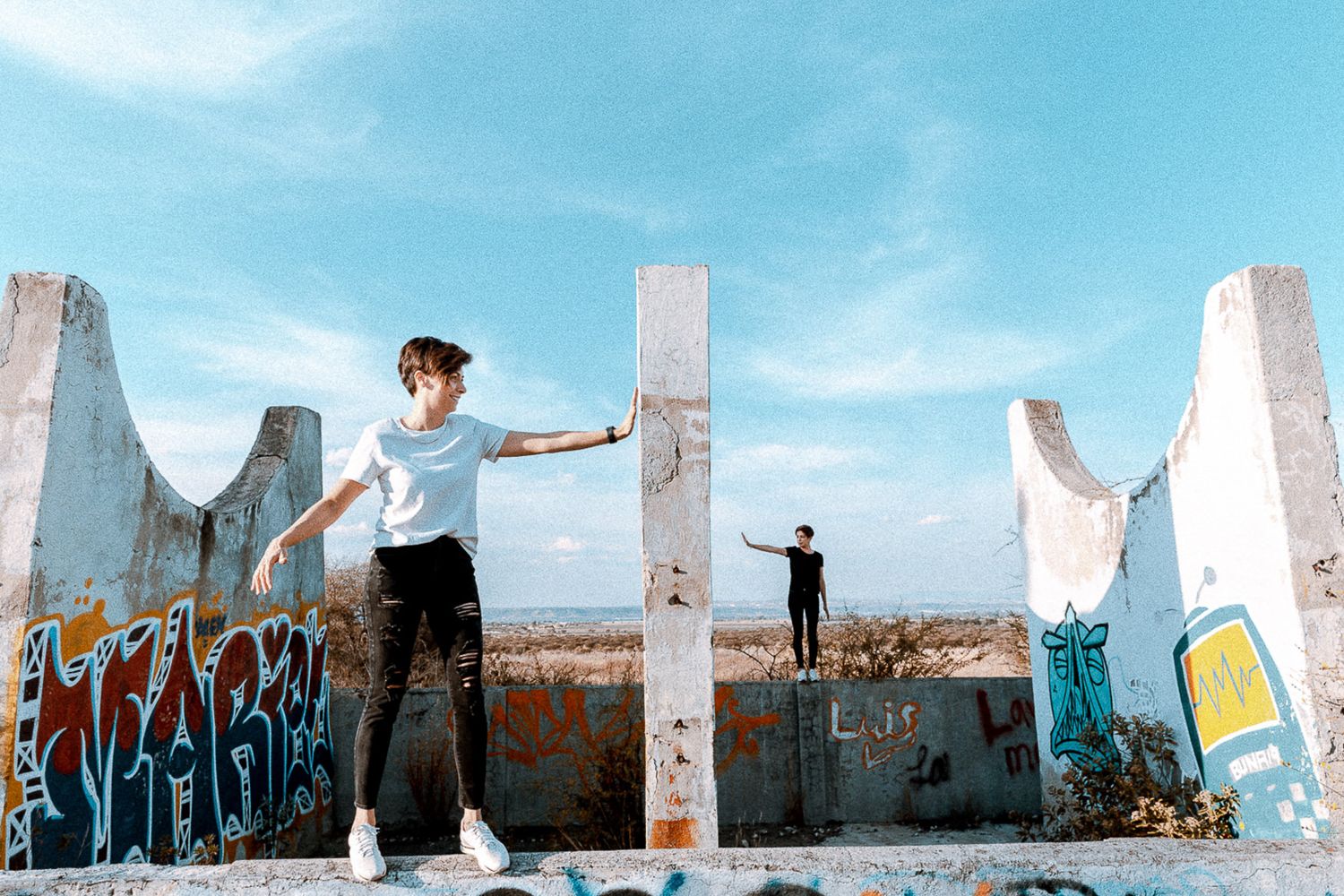 Person posing artistically among concrete ruins against blue sky.