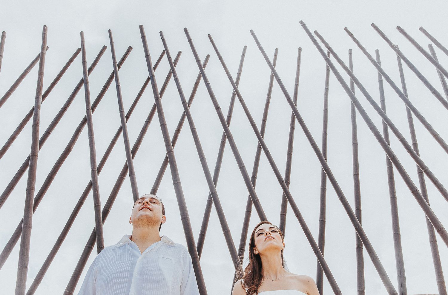 A couple looks up at geometric metal patterns against a bright sky.