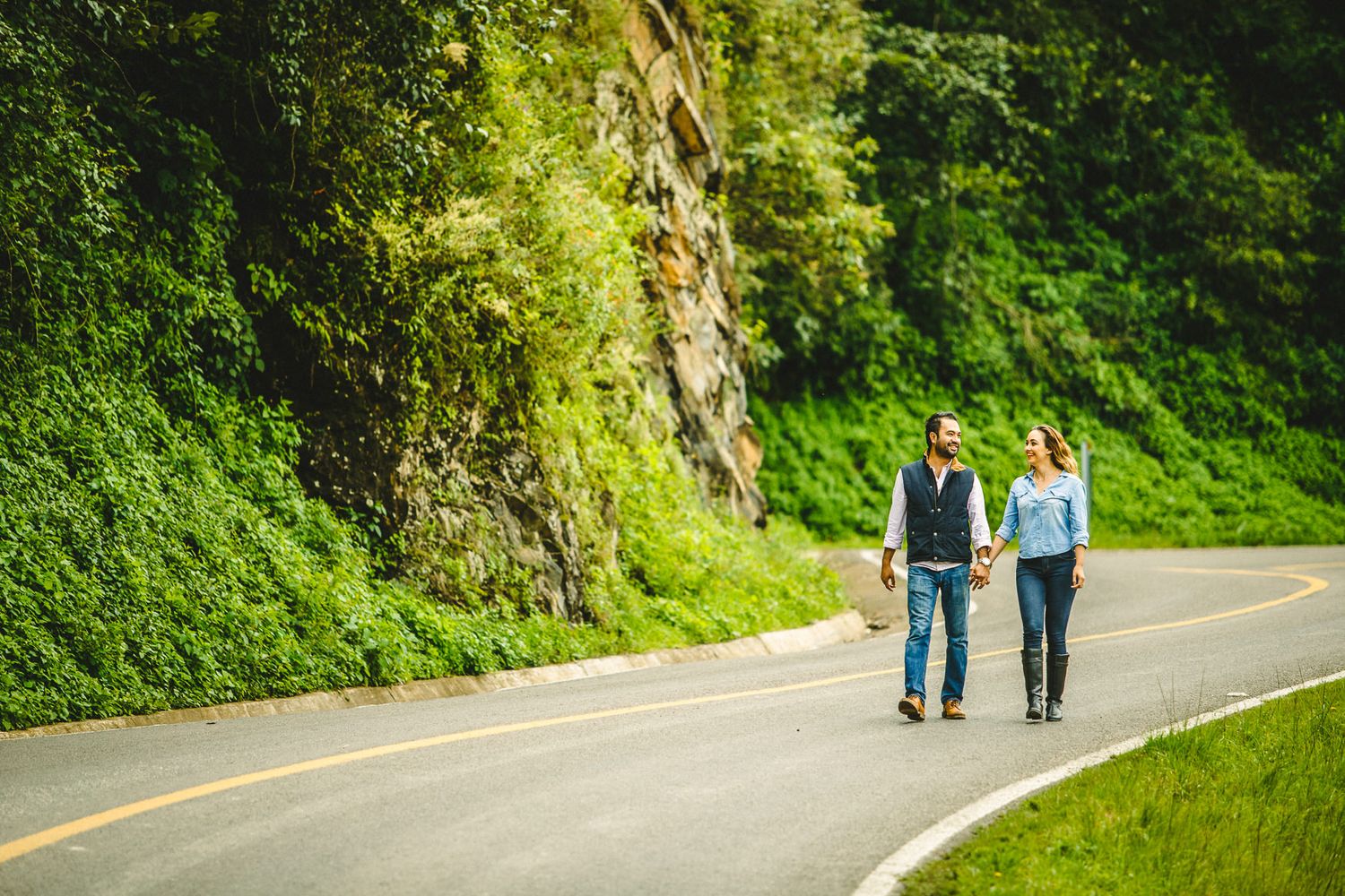 Couple walking together on scenic mountain road surrounded by lush greenery.