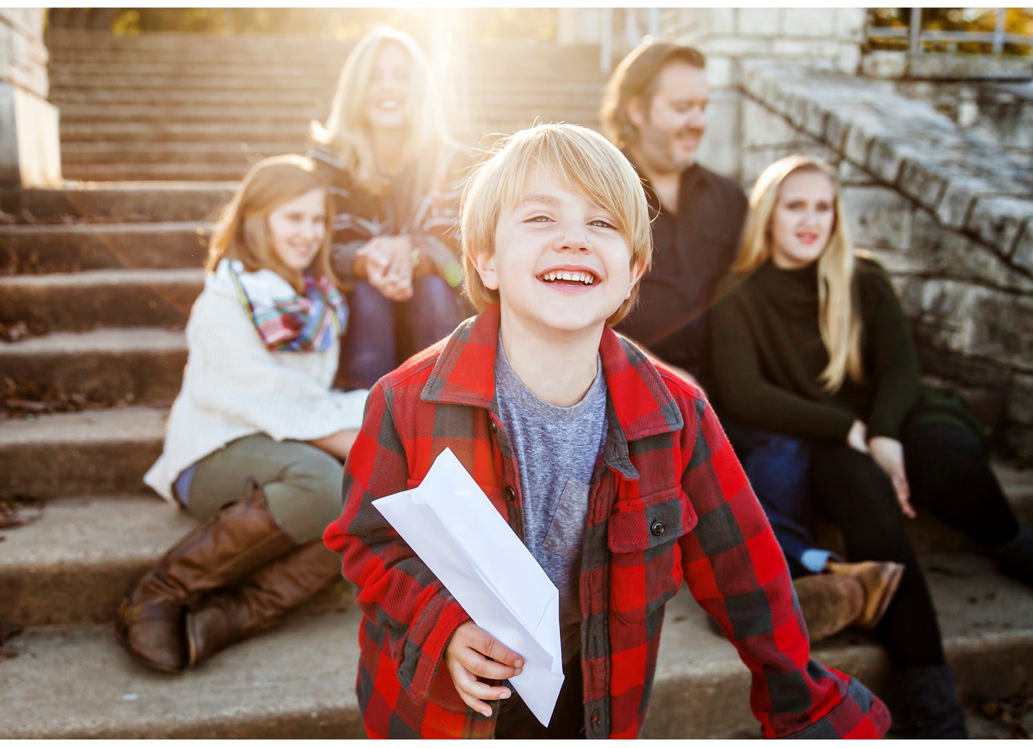 Child in red plaid jacket laughing joyfully on outdoor steps.