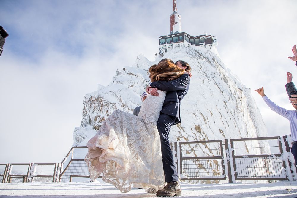 Snowy mountain summit celebration at a viewing platform with dramatic cloudy backdrop.