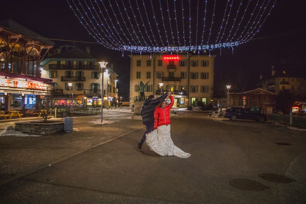 A couple stands beneath twinkling string lights in a town square at night.