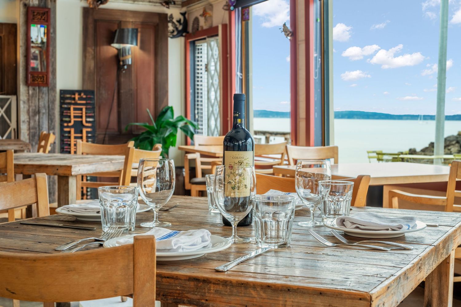 Elegant restaurant table setting with ocean view through large windows and wooden furniture.