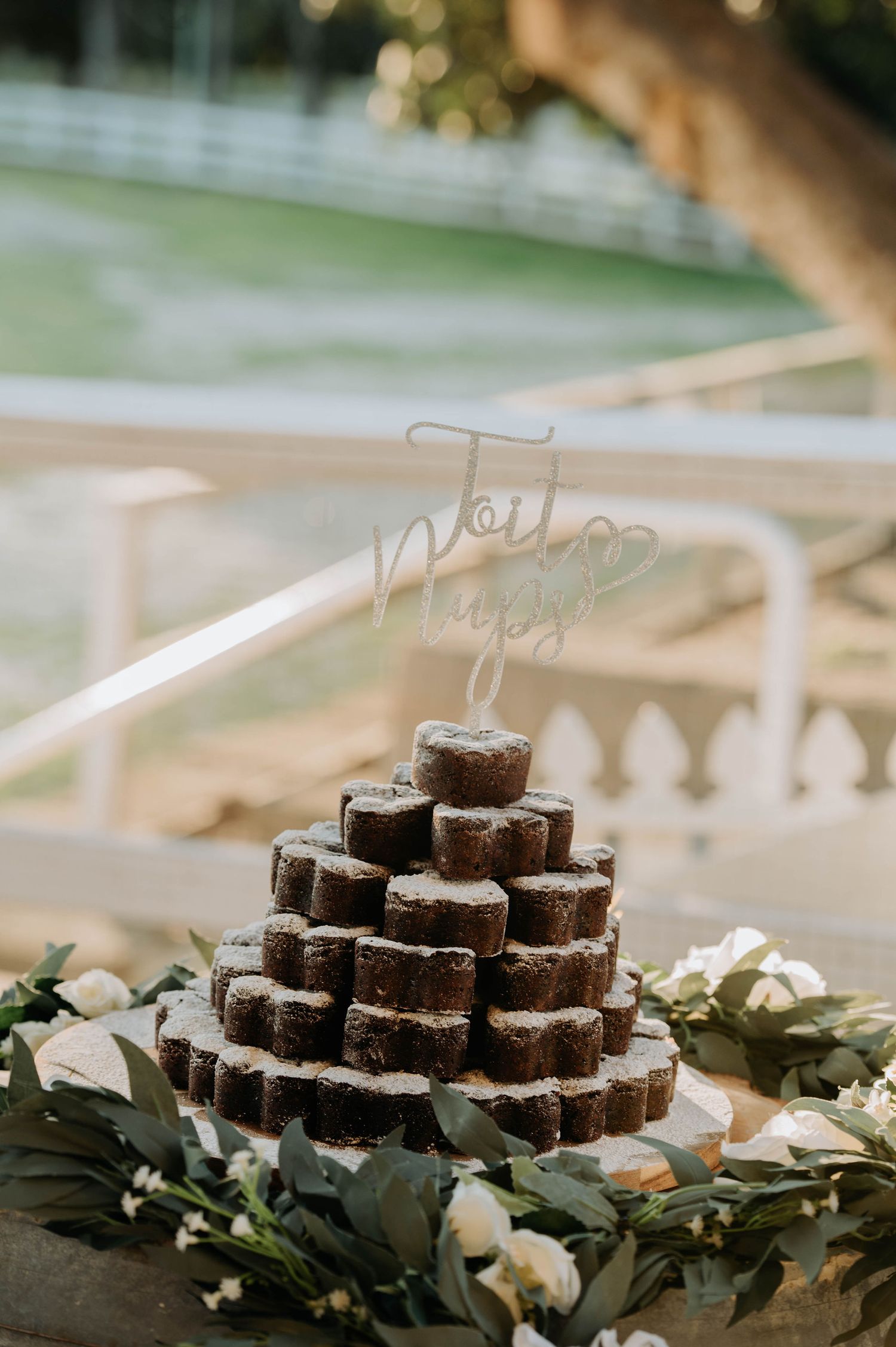 A tiered display of chocolate desserts decorated with greenery and white flowers.