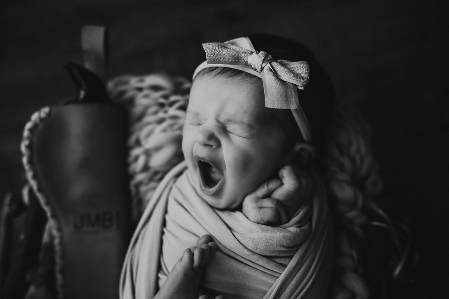 Black and white portrait of yawning baby wearing bow headband.
