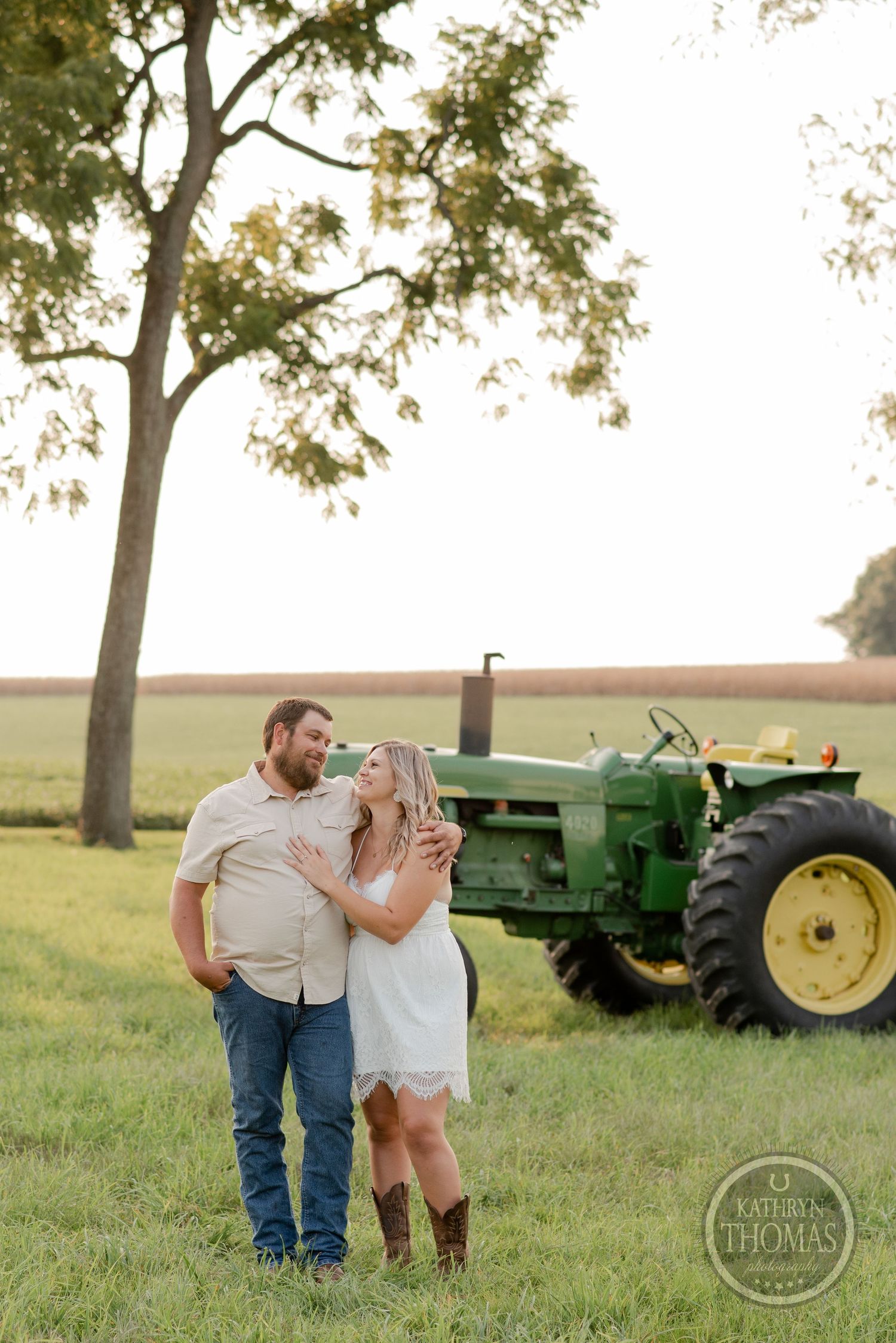 A romantic country photoshoot features a couple embracing in front of a vintage green tractor.