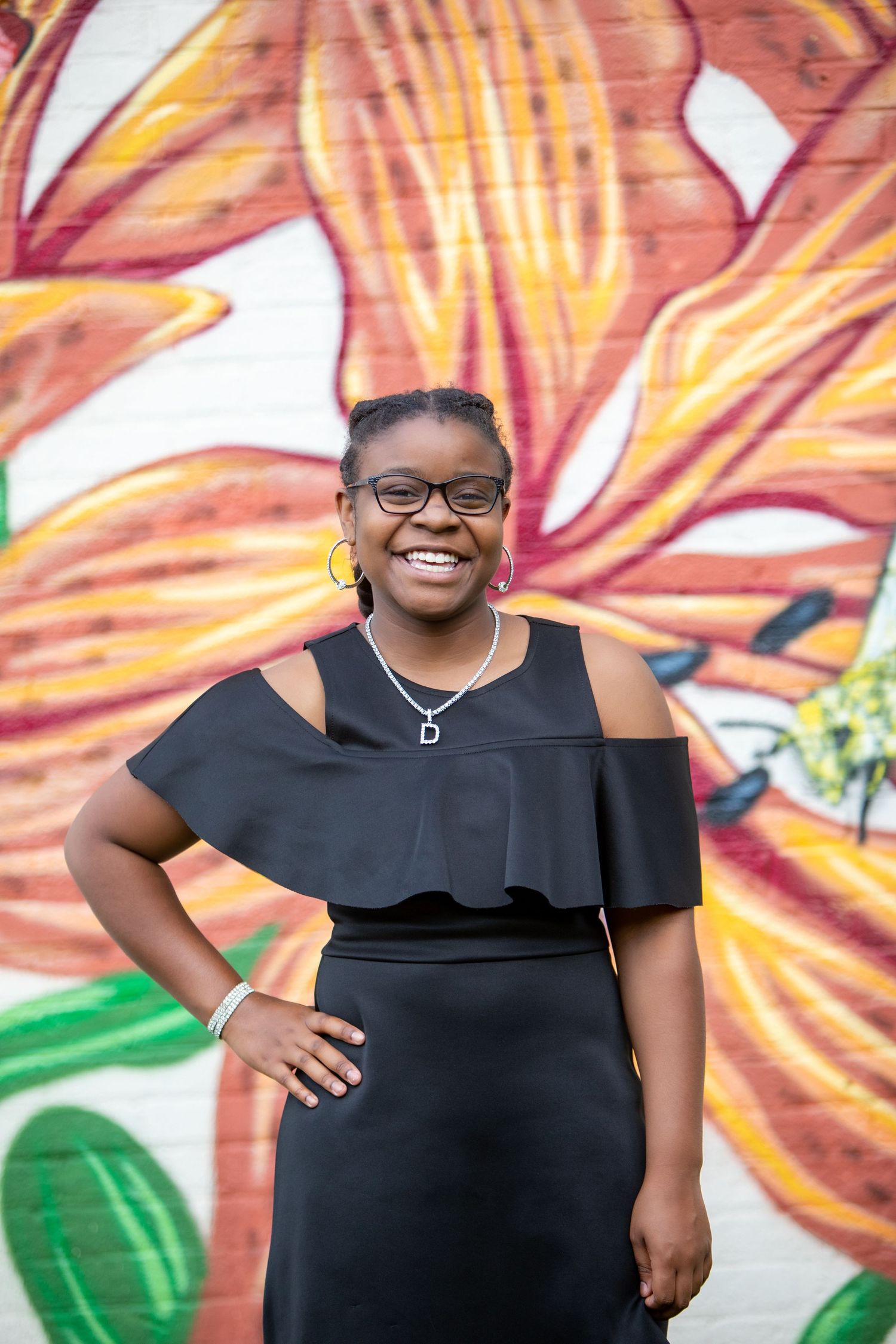 A fashionable black dress with ruffle detail is worn in front of a colorful graffiti wall background.
