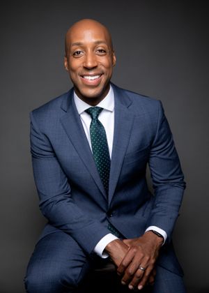 Professional portrait of Anchor for WUSA9 Lorenzo Hall in blue suit seated and smiling warmly at camera.