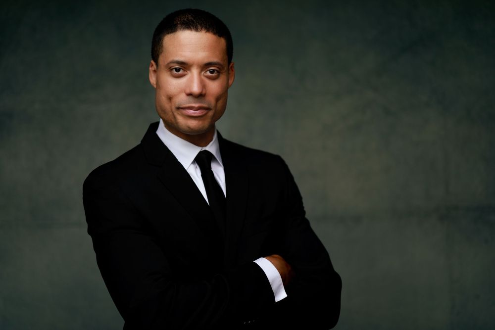 Professional portrait in black suit against moody studio backdrop.