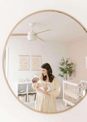 Mirror reflection shows nursery room with modern decor and person holding baby.