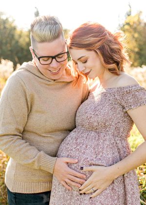 Intimate maternity moment captured in golden sunlight outdoors.