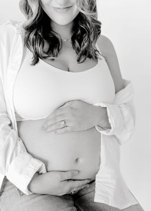 Black and white maternity photo showing pregnant belly in white shirt.