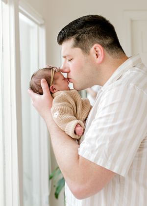 Gentle moment between newborn and caregiver by window light.