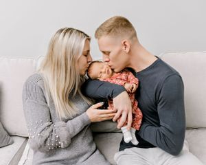 Intimate family moment with newborn on grey couch at home.