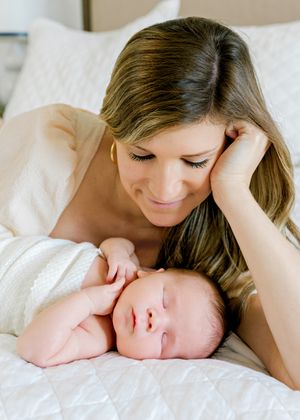 Mother and newborn sharing a peaceful moment together on white bedding.