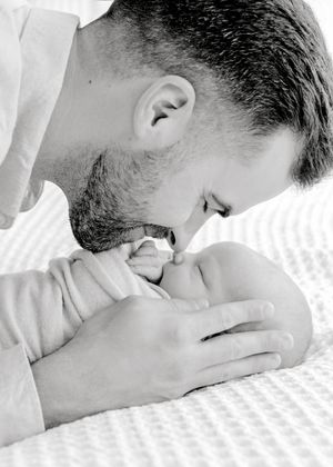 Intimate black and white photograph of parent bonding with newborn on white bedding.