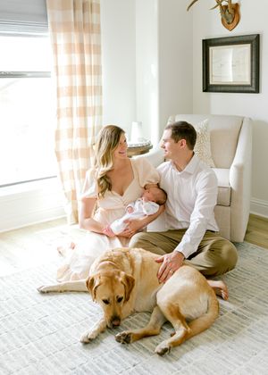Family relaxes in living room with newborn baby and golden retriever on striped rug.
