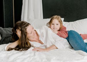 Mother and daughter sharing playful moment together on white bedding.