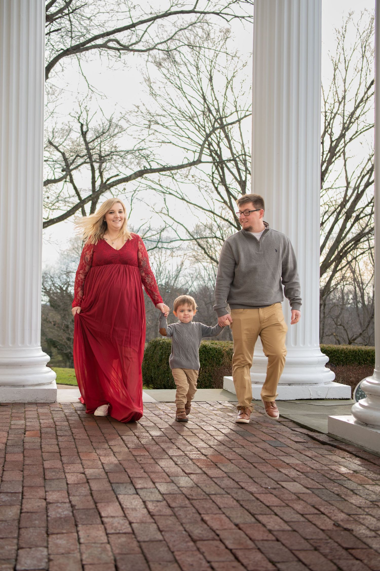 Family walks together between white columns on a brick pathway during a lifestyle photoshoot.