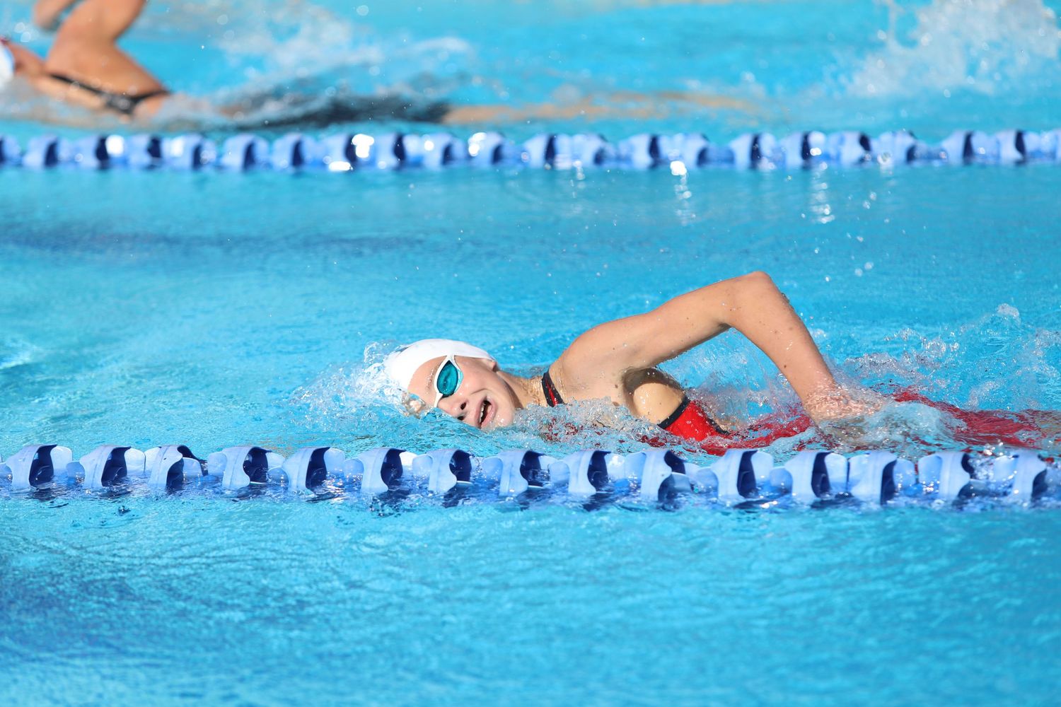 Swimmer performing freestyle stroke in a competition pool with lane dividers.