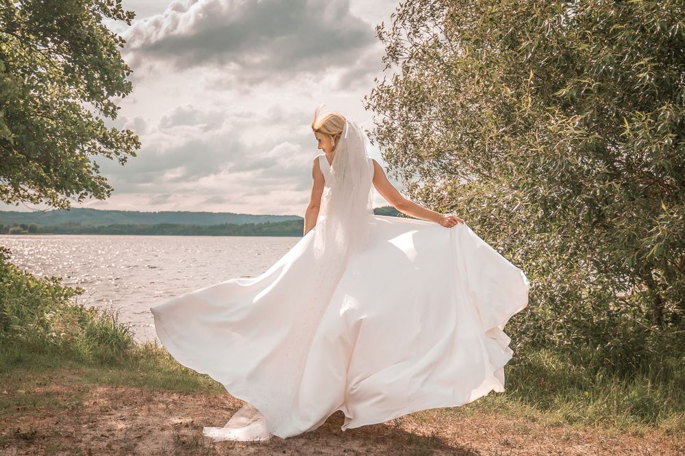 En flydende hvid brudekjole snurrer elegant mod en naturskøn baggrund ved søen på en overskyet dag.