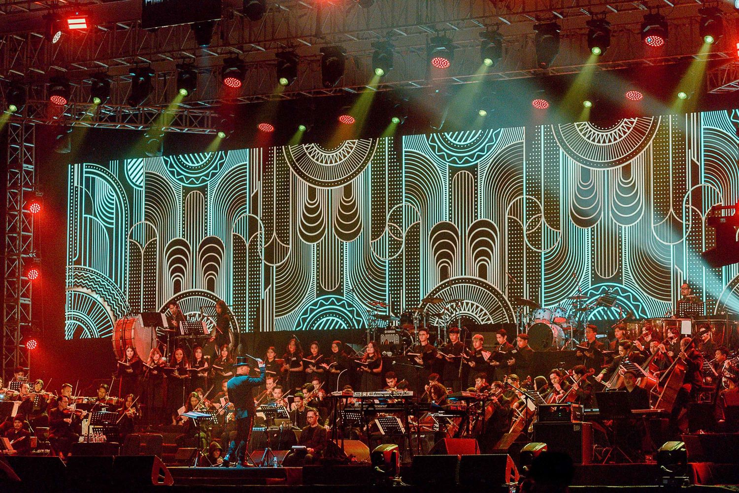 Orchestra performing on stage with ornate art deco style turquoise backdrop.