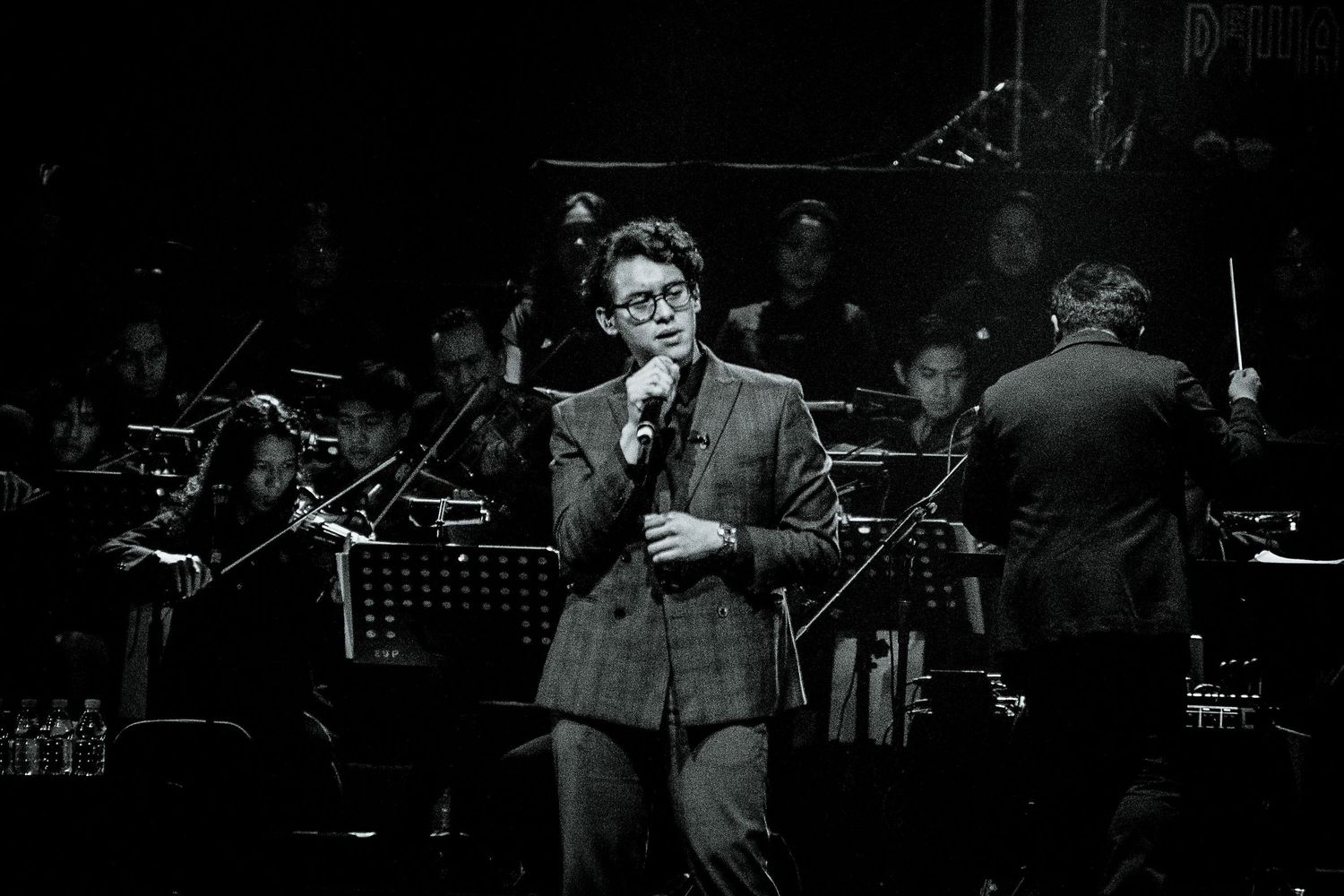 Black and white image of a performer on stage with orchestra members in the background.