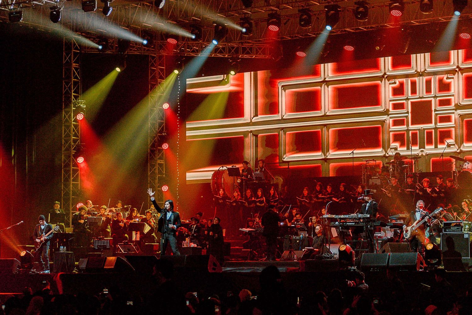 Concert stage with red lighting and geometric patterns featuring full orchestra performance.