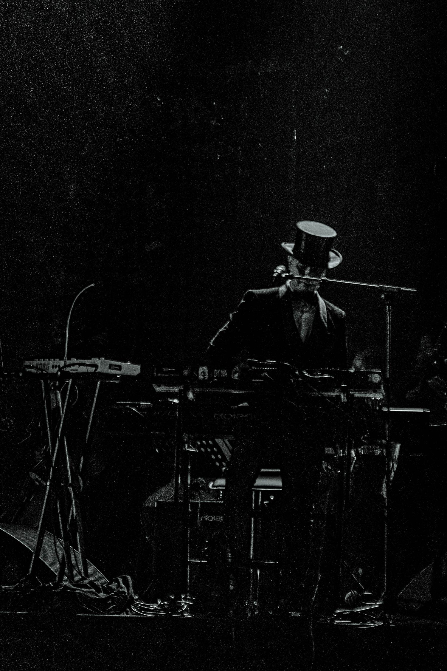 Musician performing with electronic equipment setup on dark stage with dramatic lighting.