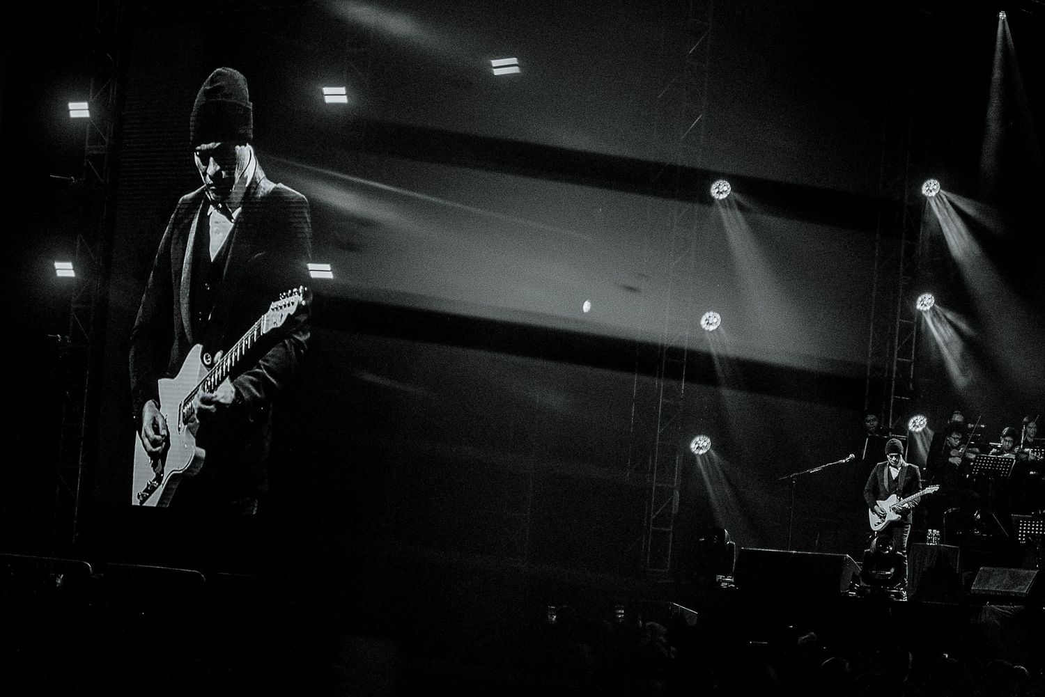 Black and white concert photo of guitarist performing on dimly lit stage.