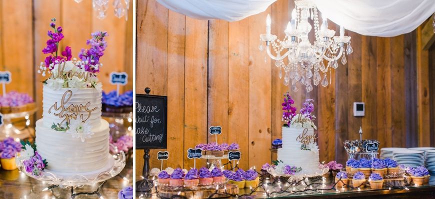 Purple and white wedding cake display with cupcakes and chandeliers in rustic wood paneled room.