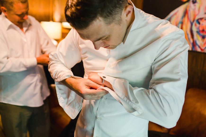 Person adjusts their sleeve cuff while getting dressed in a white formal shirt.