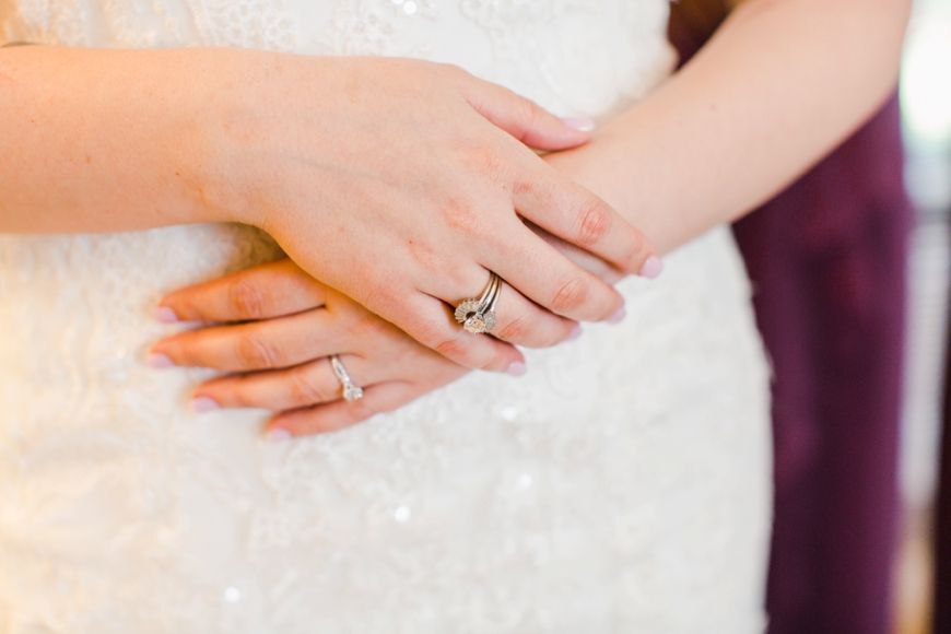 Close-up of hands showing elegant wedding rings against white lace fabric.