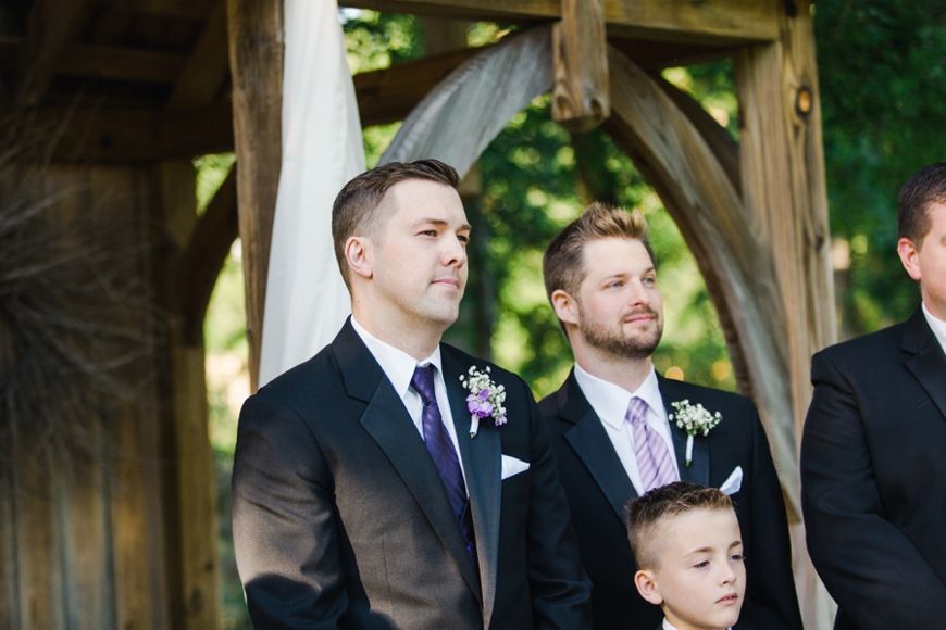 Wedding party members stand together under a rustic wooden pavilion during the ceremony.