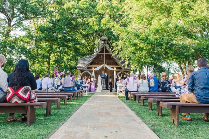 Rustic outdoor wedding chapel with wooden benches and white draping along a stone pathway.
