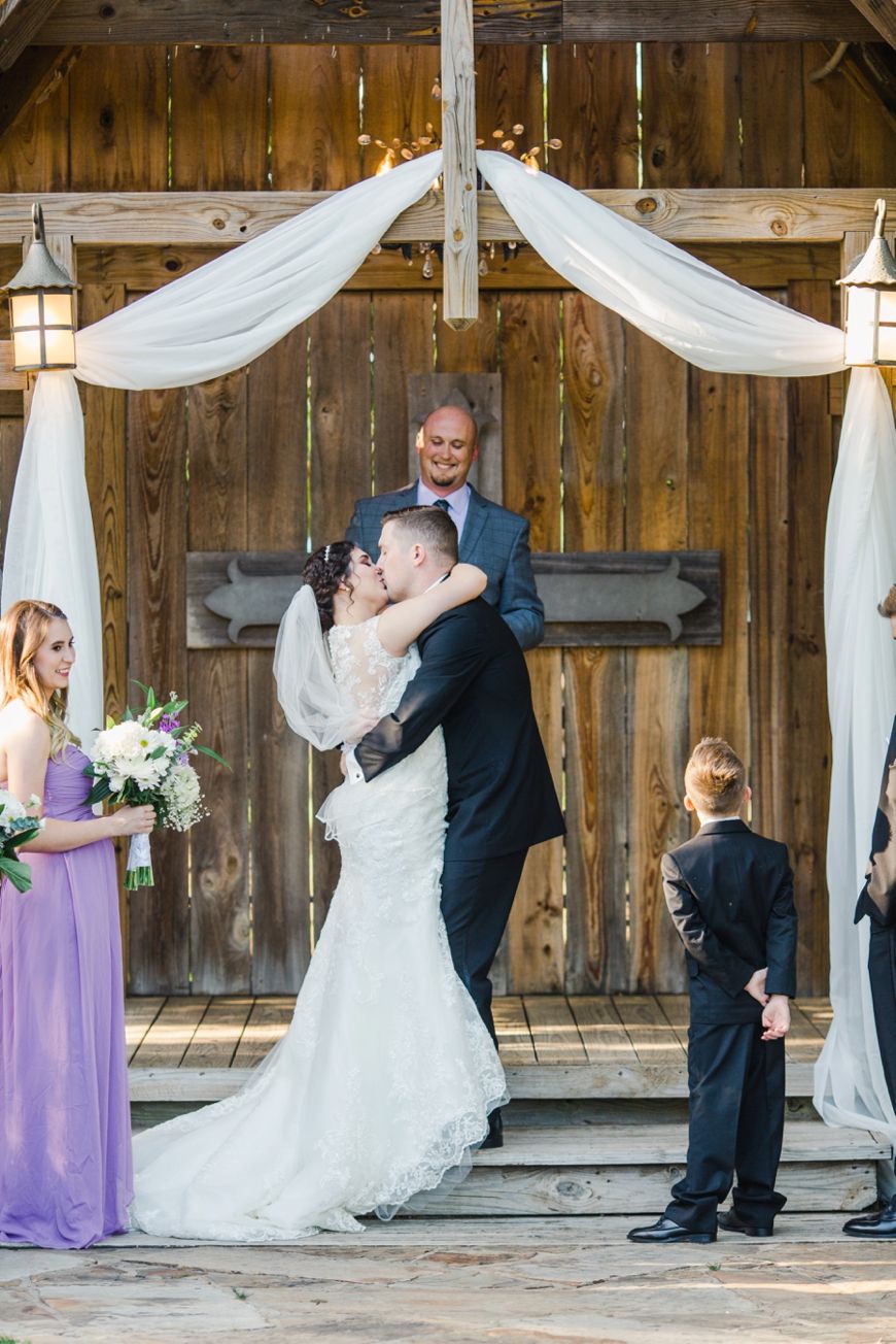 Newlyweds share their first kiss under an elegantly decorated wooden pavilion at their outdoor wedding.