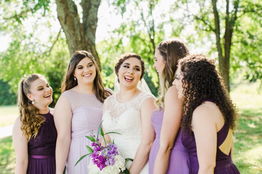 Bride and bridesmaids share joyful laughter while holding bouquets outdoors.