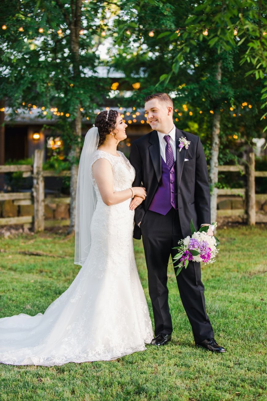 Couple laughs together during outdoor wedding portraits with string lights visible in background.